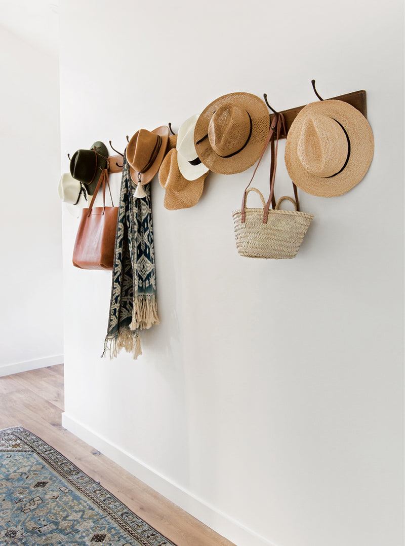 A rustic coat rack adorned with stylish hats and handbags, adding functional elegance to the entryway in "Made for Living."