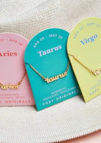 Foxy Originals Zodiac Necklaces displayed on branded cards, showcasing various gold and silver script-style pendants.