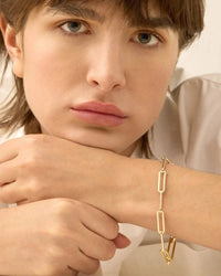 The Andi Slim Bracelet by Jenny Bird worn on the wrist of a model, showcasing its sleek paperclip design and adjustable, high-polish gold finish.