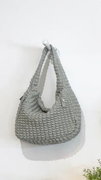 Grey vegan handbag by Pixie Mood hanging on the wall, highlighting its debossed waffle vegan leather design.