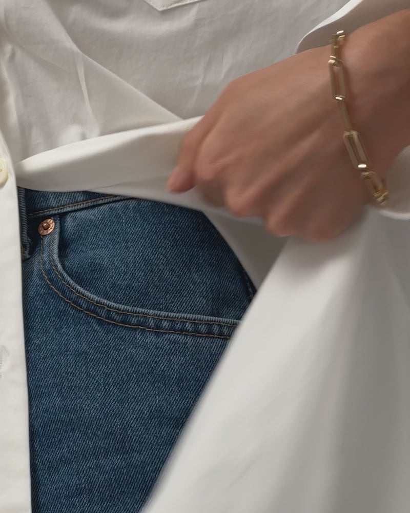 A close-up video showing the Andi Slim Bracelet by Jenny Bird worn on the wrist with the hand casually tucked in a pocket, highlighting the sleek paperclip design and high-polish gold finish.