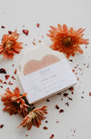 A handmade soap bar from SOAK Bath Co, partially unwrapped to reveal its luxurious, all-natural formula. Packaged in biodegradable seed paper that can be planted to grow wildflowers. Made in Canada by a woman-owned brand.