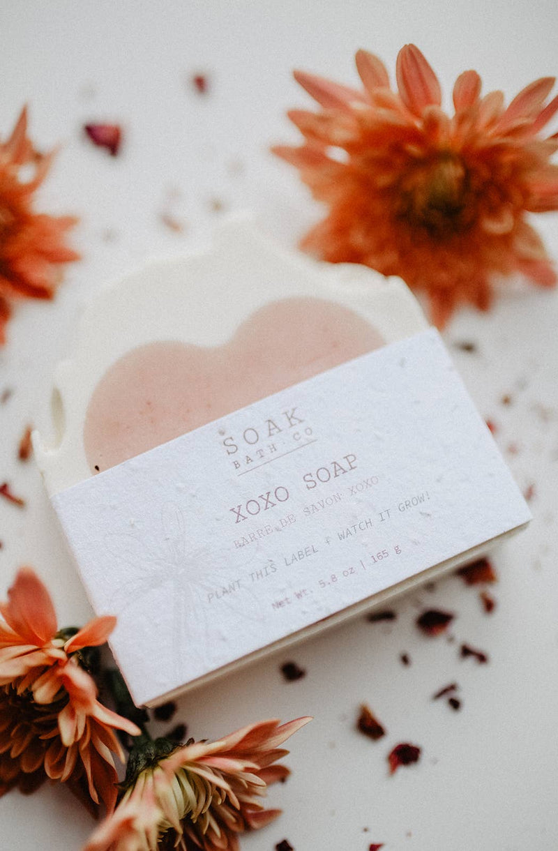 A close-up of a handmade SOAK Bath Co soap bar, partially unwrapped to highlight its smooth texture and natural ingredients. Packaged in biodegradable seed paper that can be planted to grow wildflowers. Made in Canada by a woman-owned brand.