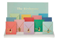 Foxy Originals Birthstone Necklace collection displayed in an elegant arrangement, showcasing gold-plated charm necklaces with colorful birthstone accents.